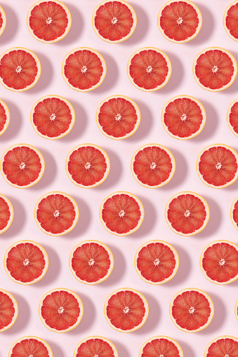 Fruit pattern with half slices of grapefruit on soft pink pastel background