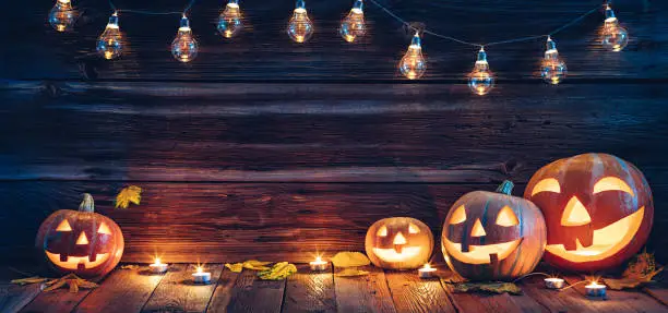 Halloween background decorated with Jack lantern pumpkins, lights and candles. Wooden wall with copy space.