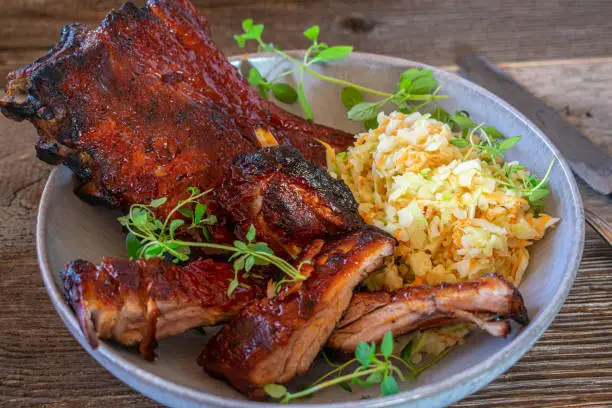 Homemade fresh and honey glazed barbecue pork ribs with a fresh coleslaw salad served on a plate on rustic and wooden table. Closeup and isolated view