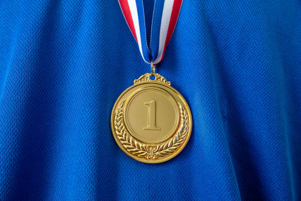 Gold medal. Champion trophy award and ribbon. Prize in sport for winner on blue shirt background Medal gold, Winner prize award hanging with red blue color ribbon on athlete chest. Golden trophy in sport for first place champion on blue color shirt background medallist stock pictures, royalty-free photos & images