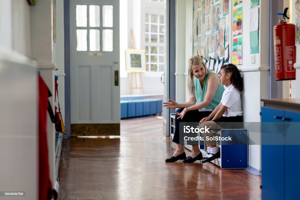 Dont Worry About It A side view a teacher and her pupil having a chat outside of the classroom of a school in Hexham in the North East of England. they are sitting together and having a discussion outside of the classroom. Teacher Stock Photo