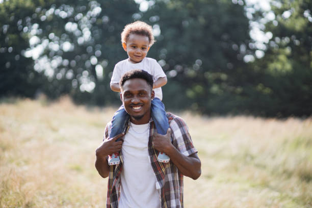 istock African man holding son on shoulders while standing on field 1340519784