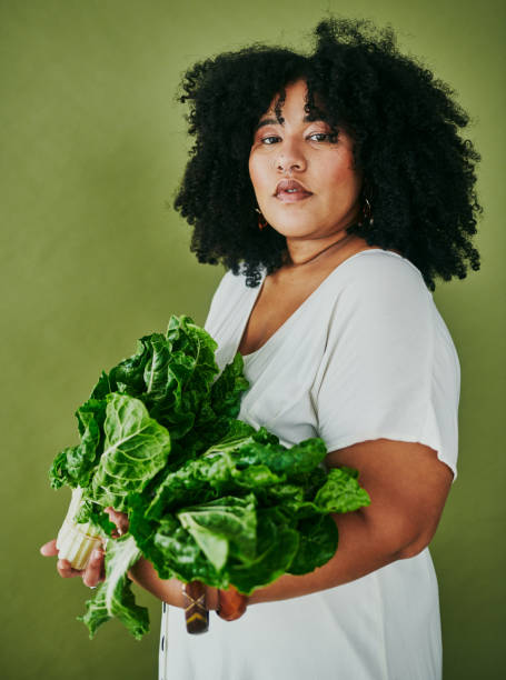 studio shot of a young woman holding a bunch of spinach against a green background - kale vegetable food leaf vegetable imagens e fotografias de stock