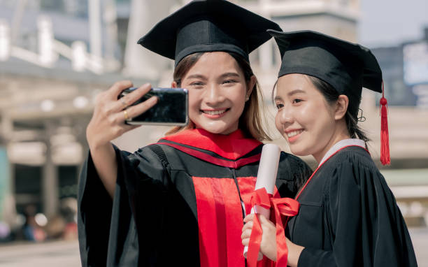 istock Two Asian female students graduated bachelor degree are taking selfie by using mobile phone while standing outdoor. Education and Technology Concept. 1340521699