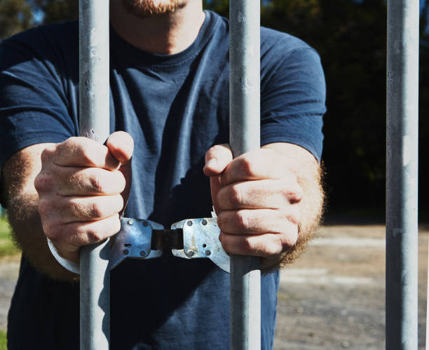 istock Man in handcuffs grips prison bars 1340525351