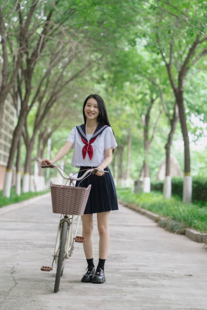 Young asian female college students, pushing bicycles and smiling