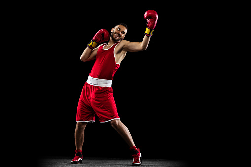 Uppercut punch. Portrait of one professional boxer in red uniform training isolated over black background. Fighter practicing in action. Health, sport, motion concept. Copy space for ad.