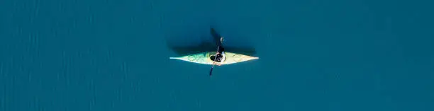 View from above, aerial view of a person paddling a canoe - kayak on the Cedrino Lake - Lago del Cedrino, surrounded by the mountain range of Supramonte located northeast of the Gennargentu massif. Sardinia, Italy.
