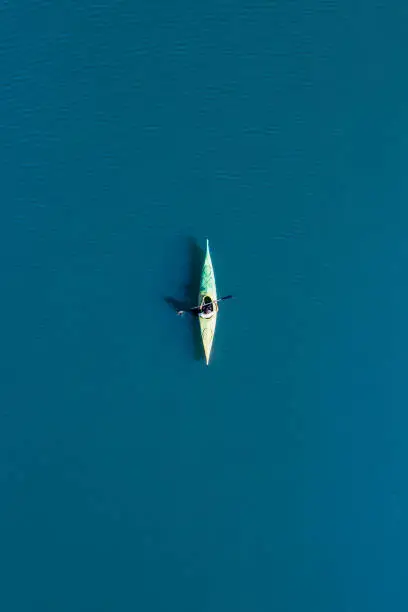 View from above, aerial view of a person paddling a canoe - kayak on the Cedrino Lake - Lago del Cedrino, surrounded by the mountain range of Supramonte located northeast of the Gennargentu massif. Sardinia, Italy.