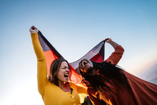 zwei multiethnische frauen mit deutscher flagge - tag der deutschen einheit stock-fotos und bilder