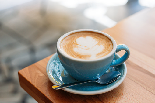 Cup of cappuccino with latte art. Coffee in blue cup on wooden table in cafe