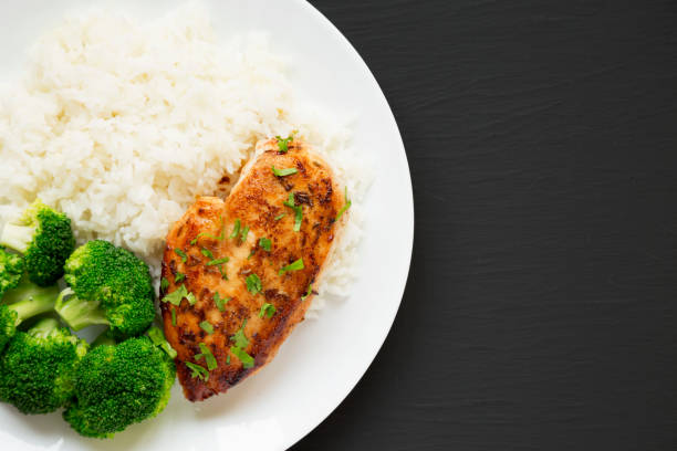istock Homemade Chicken Breast, Rice and Broccoli on a white plate on a black surface, top view. Flat lay, overhead, from above. Space for text. 1340542317