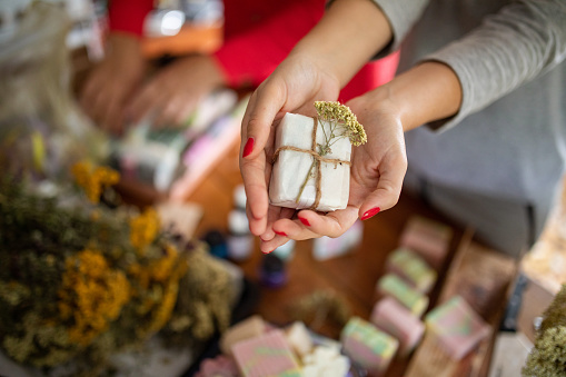 Young woman holding packed handmade soaps from natural oils at her home workshop