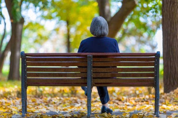 istock Aged woman sitting on bench in park 1340543507