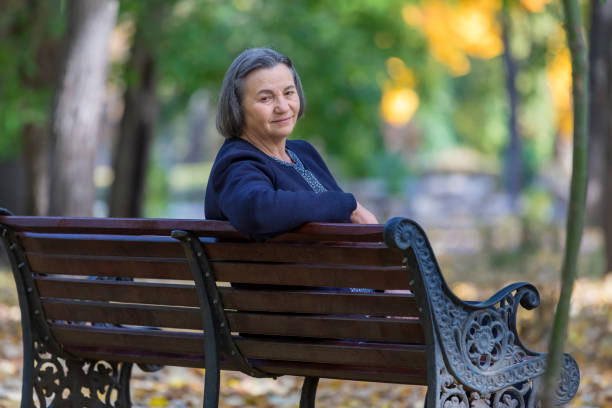 istock Aged woman sitting on bench in park 1340543523