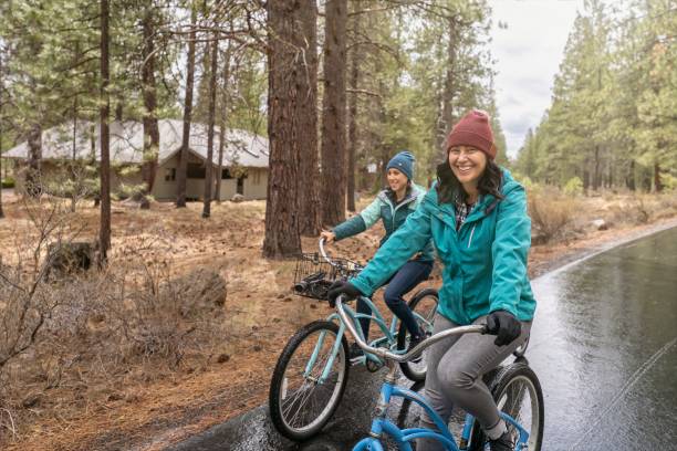 irmãs adultas mestiças em um passeio de bicicleta divertido e relaxante na chuva - cycling bicycle healthy lifestyle green - fotografias e filmes do acervo