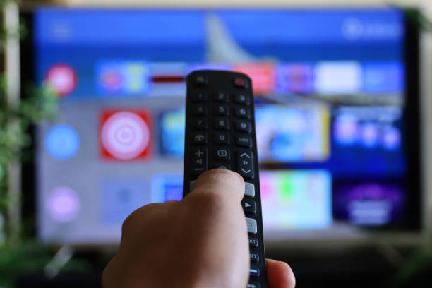 istock Image of unrecognisable person's hand holding a TV remote control, pointing at television screen, changing channels from rows of Smart Television Screen App Icons, background 1340551907