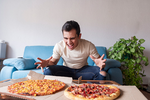 Average age 25-year-old Latino man in his living room with a shocked expression upon seeing his two boxes of pizza