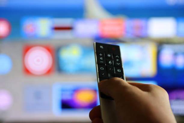 istock Image of unrecognisable person's hand holding a TV remote control, pointing at television screen, changing channels from rows of Smart Television Screen App Icons, background 1340551955