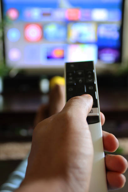 istock Image of unrecognisable person's hand holding a TV remote control, pointing at television screen, changing channels from rows of Smart Television Screen App Icons, legs stretched on coffee table 1340552076