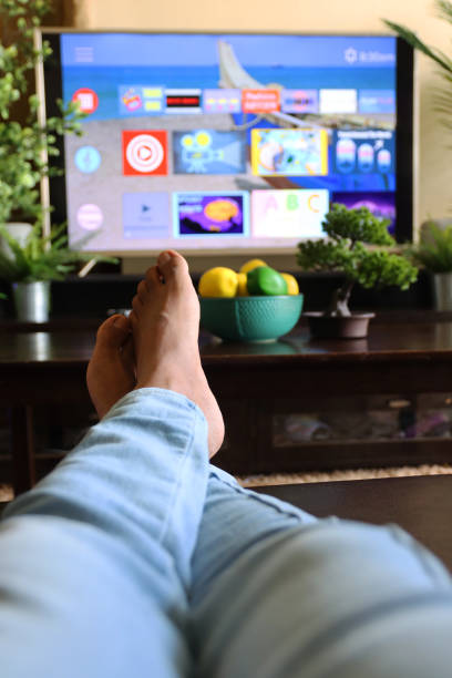 istock Image of unrecognisable person's legs on coffee table in front of Smart Television with rows of Screen App Icons, domestic life concept 1340552081