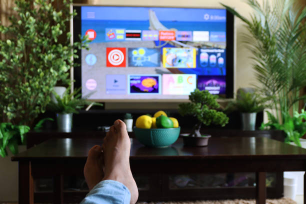 istock Image of unrecognisable person's feet on coffee table in front of Smart Television with rows of Screen App Icons, domestic life concept 1340552122