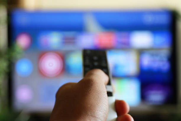 istock Image of unrecognisable person's hand holding a TV remote control, pointing at television screen, changing channels from rows of Smart Television Screen App Icons, background 1340552164