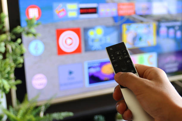 istock Image of unrecognisable person's hand holding a TV remote control, pointing at television screen, changing channels from rows of Smart Television Screen App Icons, background 1340552198