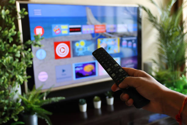 istock Image of unrecognisable person's hand holding a TV remote control, pointing at television screen, changing channels from rows of Smart Television Screen App Icons, background 1340552213