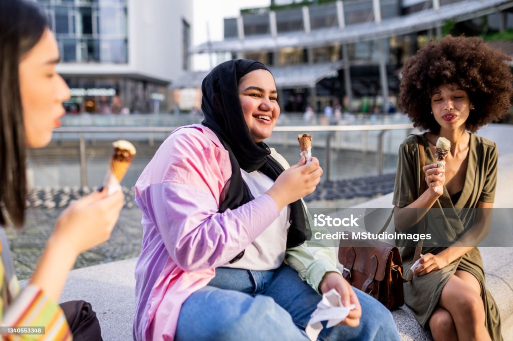 Tre amici seduti all'aperto e mangiando un gelato - Foto stock royalty-free di Gelato