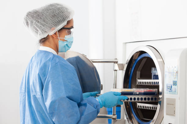 young female scientist sterilizing laboratory material in autoclave - equipamento médico imagens e fotografias de stock