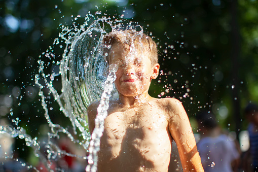 A little boy enjoys the cold waters of a fountain during the heat wave. Conceptual photography of hot weather, heat wave, global warming, summer season, climate change, enjoy life.