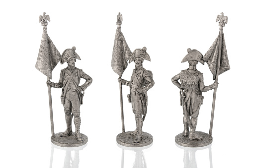 Miniature figure statuettes of tin soldier of revolutionary 18th century, unpainted gray, three angles on white background. Ancient toy Use for military reconstruction. Close up selective soft focus.