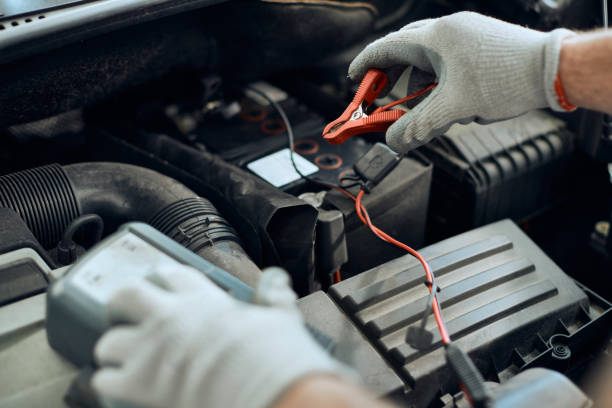 istock Close-up of auto mechanic attaching jumper cables while checking car battery in workshop. 1340556279