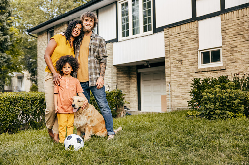 Family portrait of a smiling couple, kid and dog all embracing and looking at camera.