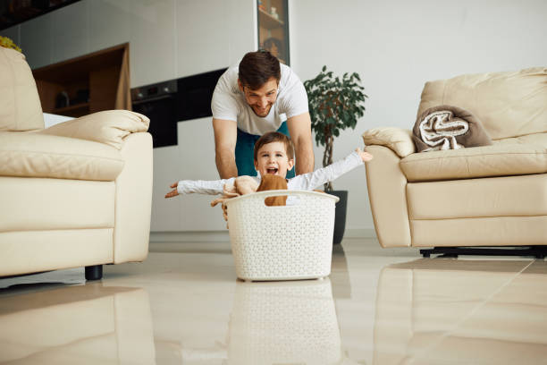 istock Happy kid with arms outstretched having fun while father is pushing him in laundry basket at home. 1340560707