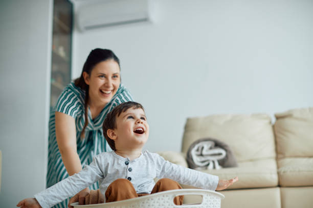 istock Cheerful boy having fun with his mother while she pushes him in laundry basket around the house. 1340560737
