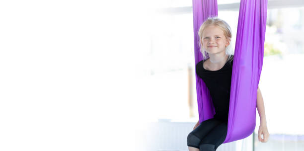 баннер дети воздушные летающие упражнения йоги. портрет молодой улыбающейся девушки практикуется в аэро растяжке, качели в фиолетовом гам� - child swing swinging balance стоковые фото и изображения