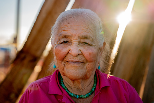 Portrait of Elderly Navajo Native American Woman smiling outside in her yard on a sunny day wearing authentic Navajo Turquoise Jewelry