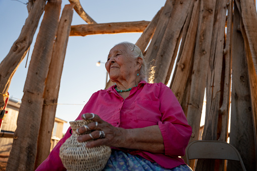 Portrait of Elderly Navajo Native American Woman smiling outside in her yard on a sunny day wearing authentic Navajo Turquoise Jewelry and homemade basket