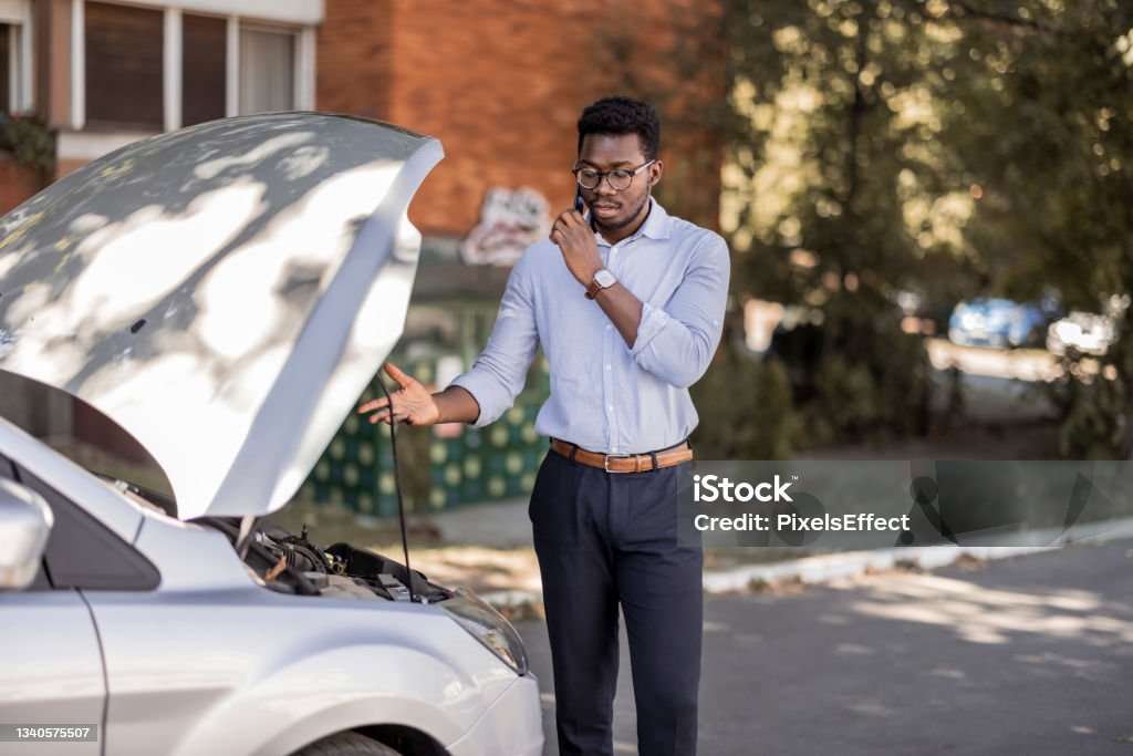 How long will it take for someone to come and help? Young African American man calling for car service Roadside Assistance Stock Photo