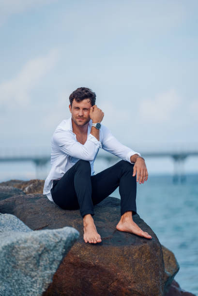 istock Content stylish man on rock near sea 1340585544