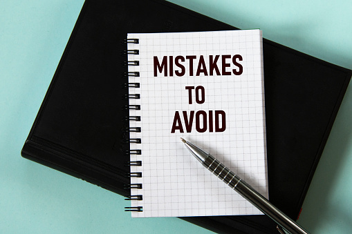 MISTAKES TO AVOID - words in a white notebook against the background of a black notebook with a pen