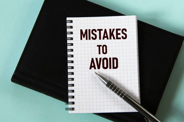 MISTAKES TO AVOID - words in a white notebook against the background of a black notebook with a pen.