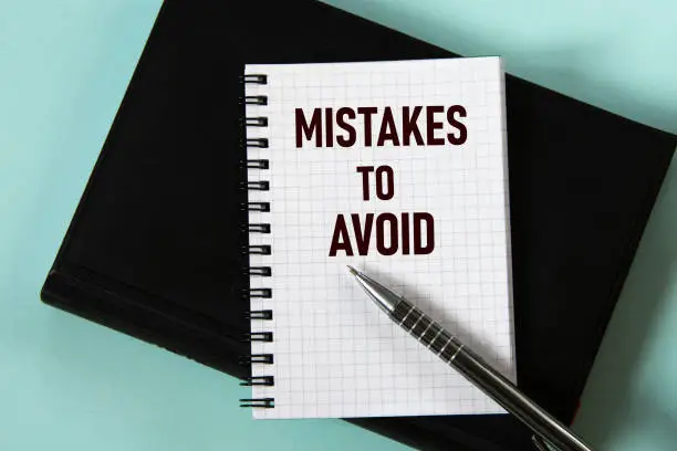 MISTAKES TO AVOID - words in a white notebook against the background of a black notebook with a pen. Business concept