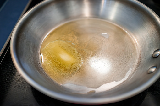 Grass-fed butter melting in stainless steel frying pan at high heat closeup for cooking sauteing