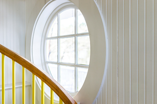 Closeup of vintage room in house with spiral winding staircase and small round window and French country panel white walls