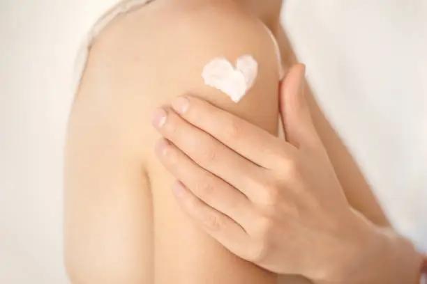 A young girl applies a moisturizer to her skin, a woman gently cares for her body, depicts a heart with a cream, taking care of herself, beauty and health.