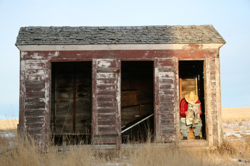 A Caucasian man reading a newspaper in an outhouse. Man is sitting in a bathroom in a rural setting and going to the bathroom. Man is wearing cowboy hat and squatting. He is unrecognizable. Image taken near Calgary, Alberta, Canada. 