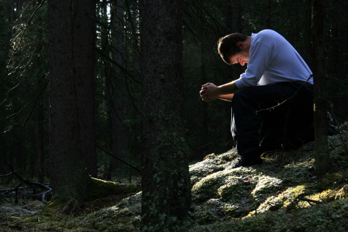 A man prays in the forest.